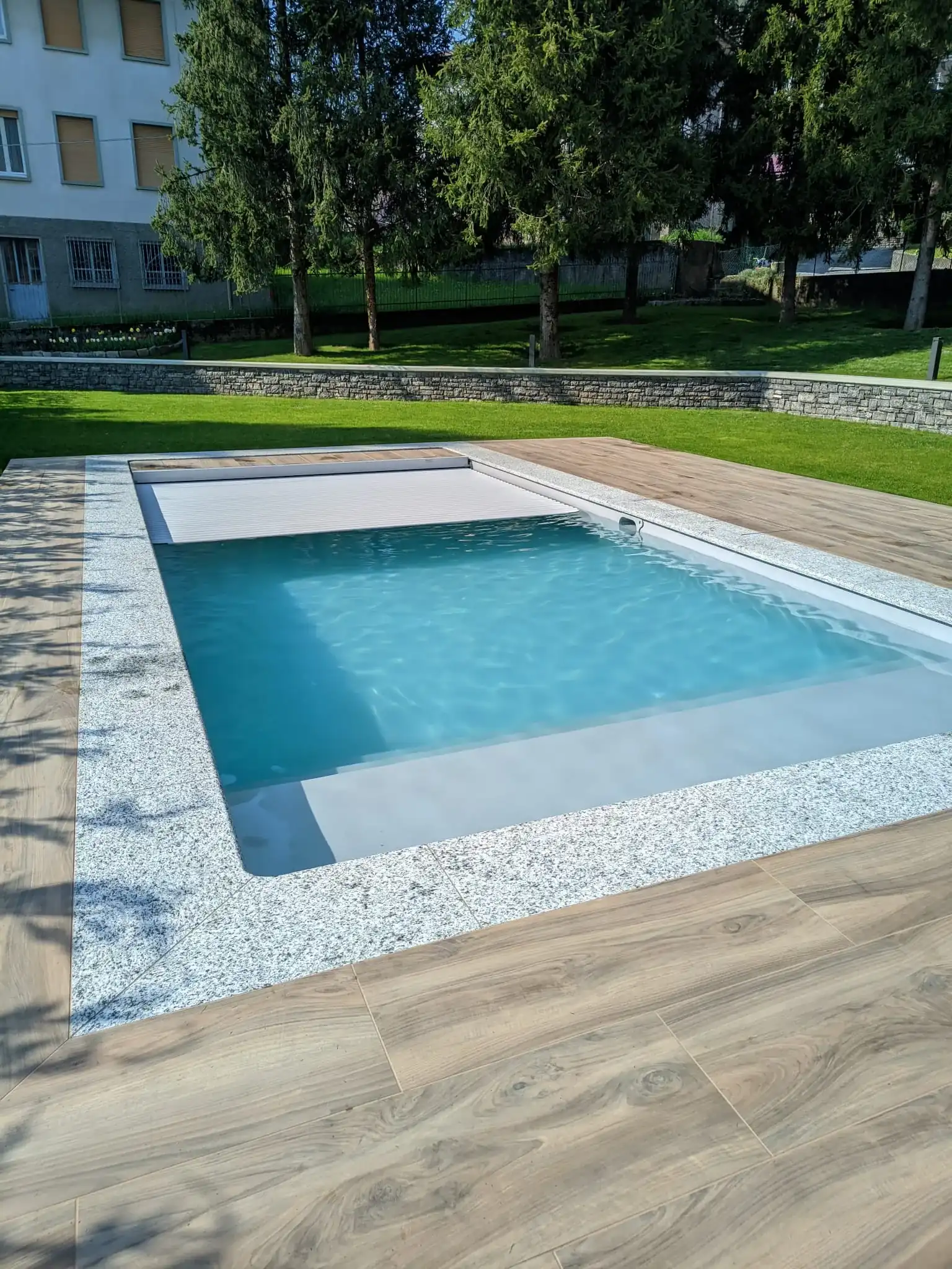 Piscina con deck in gres effetto legno e copertura a lamelle